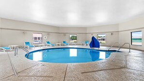 Una piscina interior con sillas azules, una sombrilla azul y vistas al exterior.