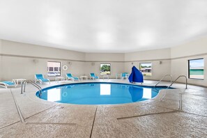Una piscina interior con sillas azules, una sombrilla azul y vistas al exterior.