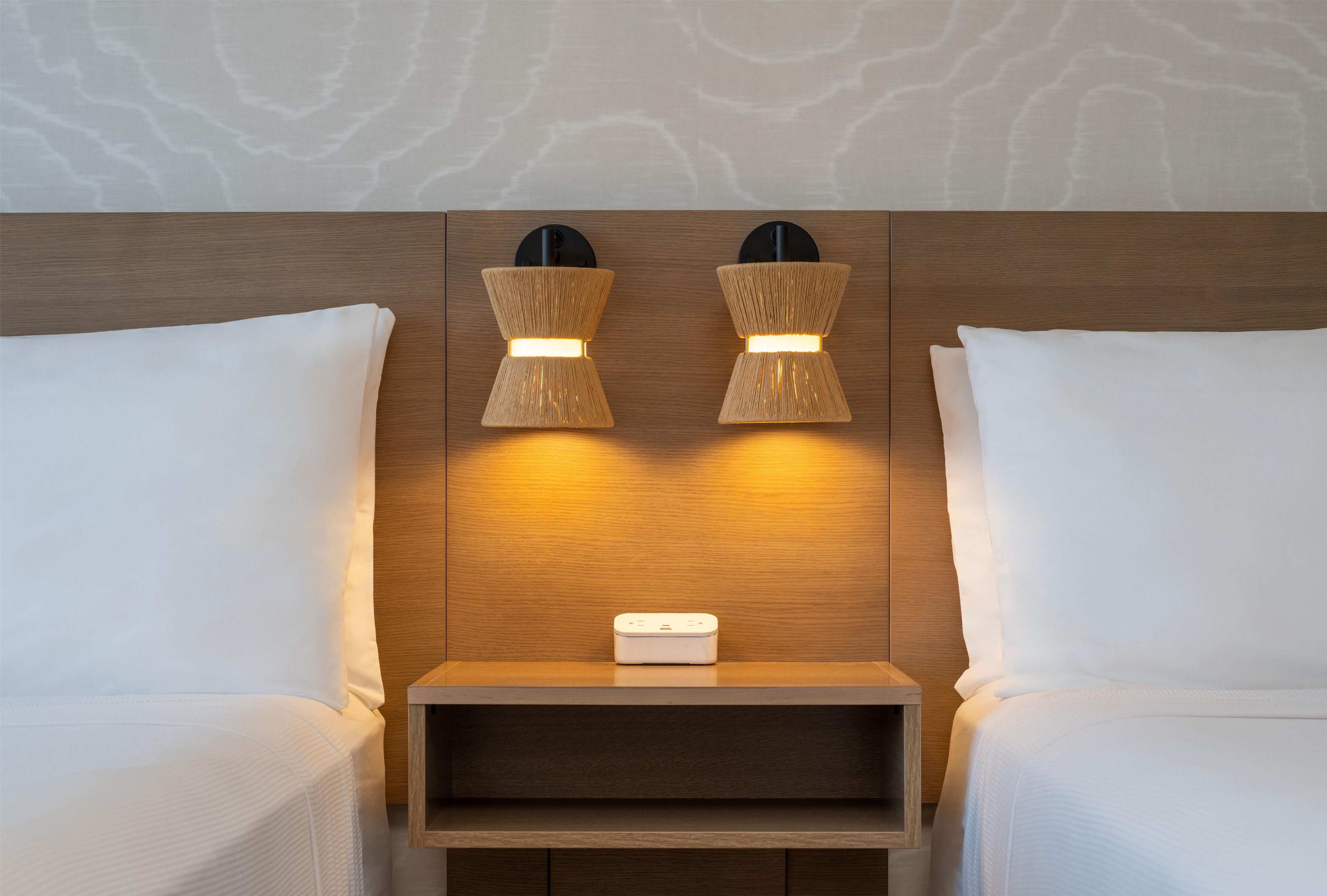 Una habitación de hotel con dos camas, una mesita de noche y una lámpara fijada a la pared.