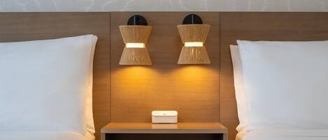 Una habitación de hotel con dos camas, una mesita de noche y una lámpara fijada a la pared.