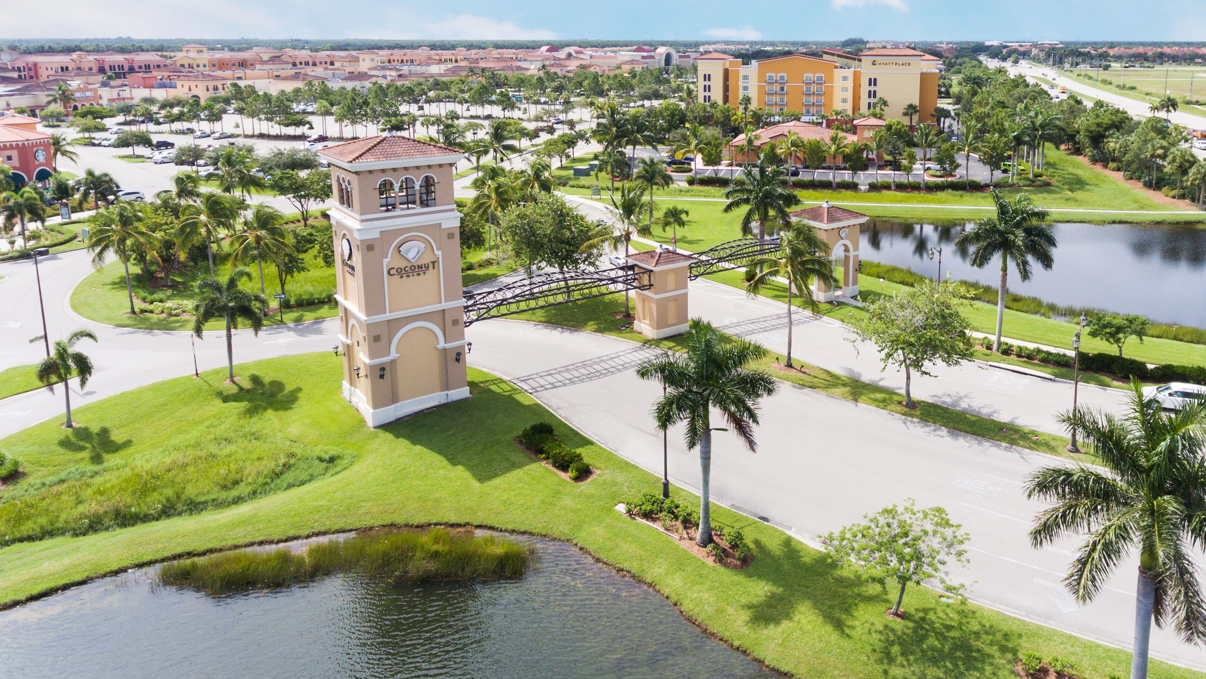 A gated entrance with a clock tower, palm trees, and a body of water.