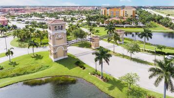 A gated entrance with a clock tower, palm trees, and a body of water.