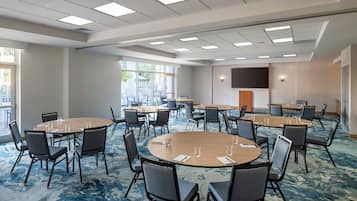 A conference room with multiple tables and chairs, large windows, and a flat-screen TV mounted on the wall.