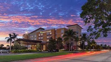 Un hotel de varios pisos con un llamativo letrero de 'Hyatt Place', rodeado de palmeras y un césped bien cuidado.