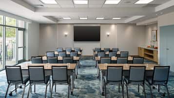 Une salle de conférence équipée de plusieurs tables et chaises, d’un grand écran et offrant une vue sur l’extérieur.
