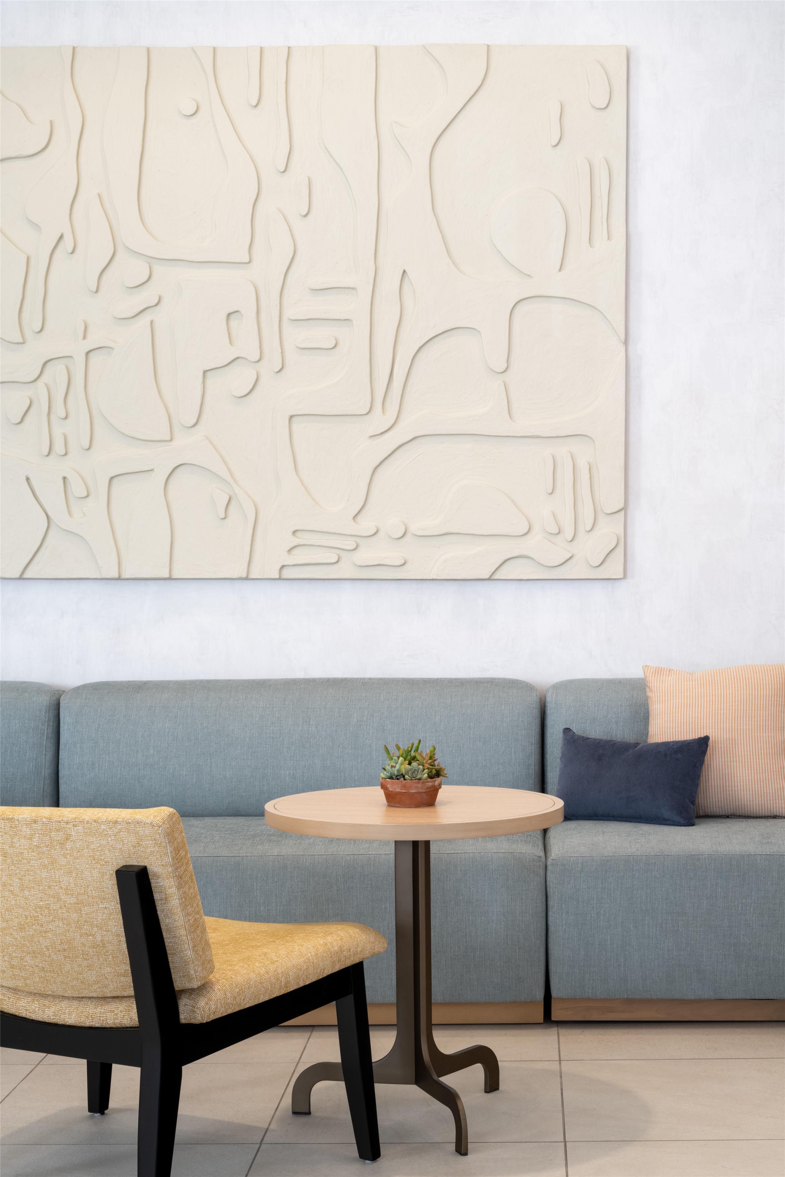 A modern living room with a grey sofa, a round wooden coffee table, and a woven chair.