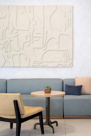Una sala moderna con un sofá gris, una mesa de centro redonda de madera y una silla trenzada.