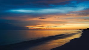 A beach at sunset with calm waters reflecting the sky.