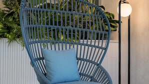 A blue woven chair with a cushion, a small round table, and a tall floor lamp with two spherical lights.