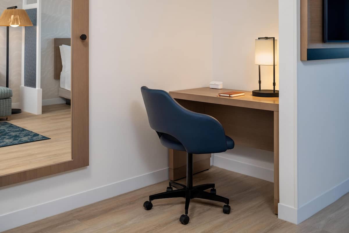 Una habitación de hotel moderna con un escritorio de madera, una silla de oficina azul, una lámpara y un televisor de pantalla plana montado en la pared.