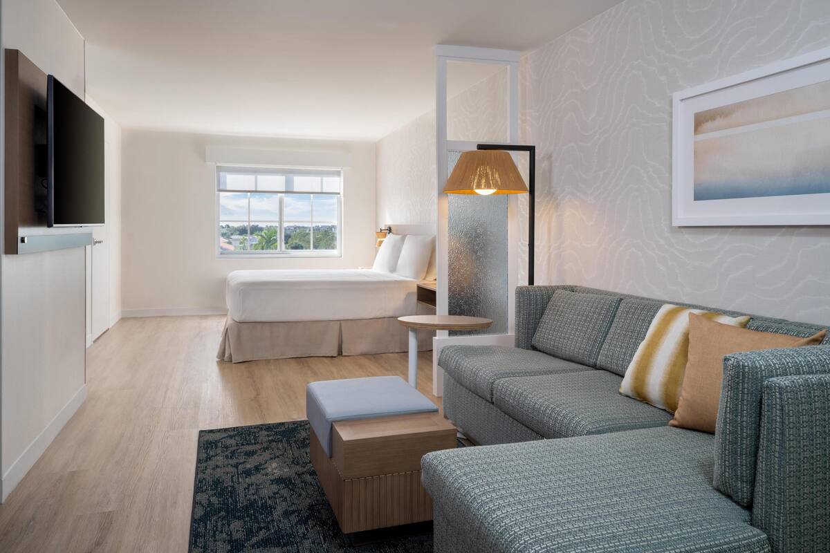 Una habitación de hotel moderna con cama, sofá, mesita, lámpara y televisor.