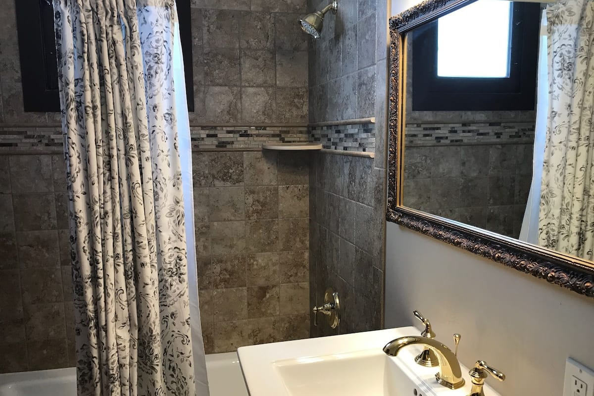 A bathroom with a white bathtub, a gold faucet, a large mirror with an ornate frame, and a shower area with a glass door.