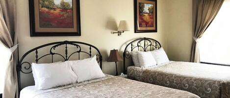 A hotel room with two beds, each with a patterned bedspread, a ceiling fan, and two framed paintings on the walls.