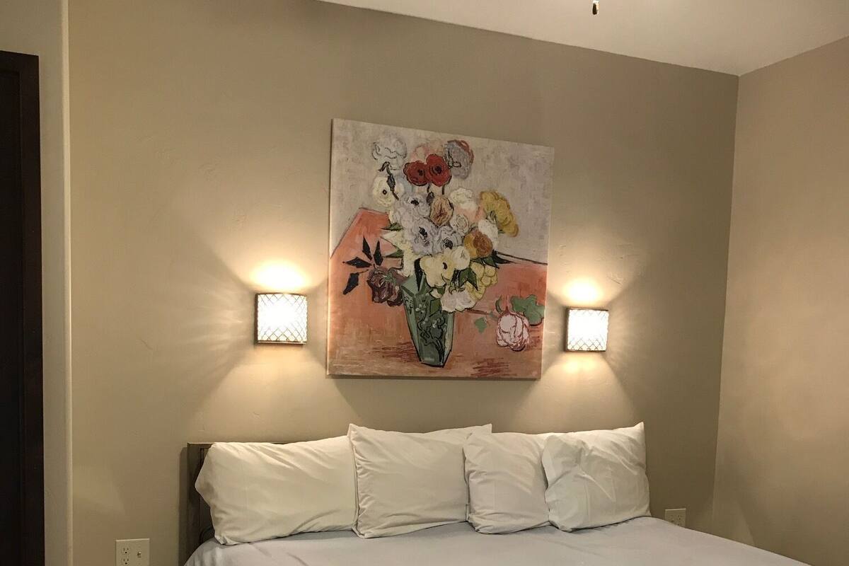 A bedroom with a bed, a ceiling fan, and a painting of flowers on the wall.