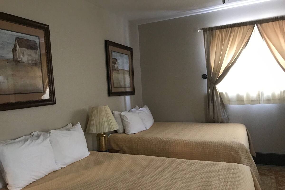 A hotel room with two beds, a lamp, and two framed pictures on the wall.