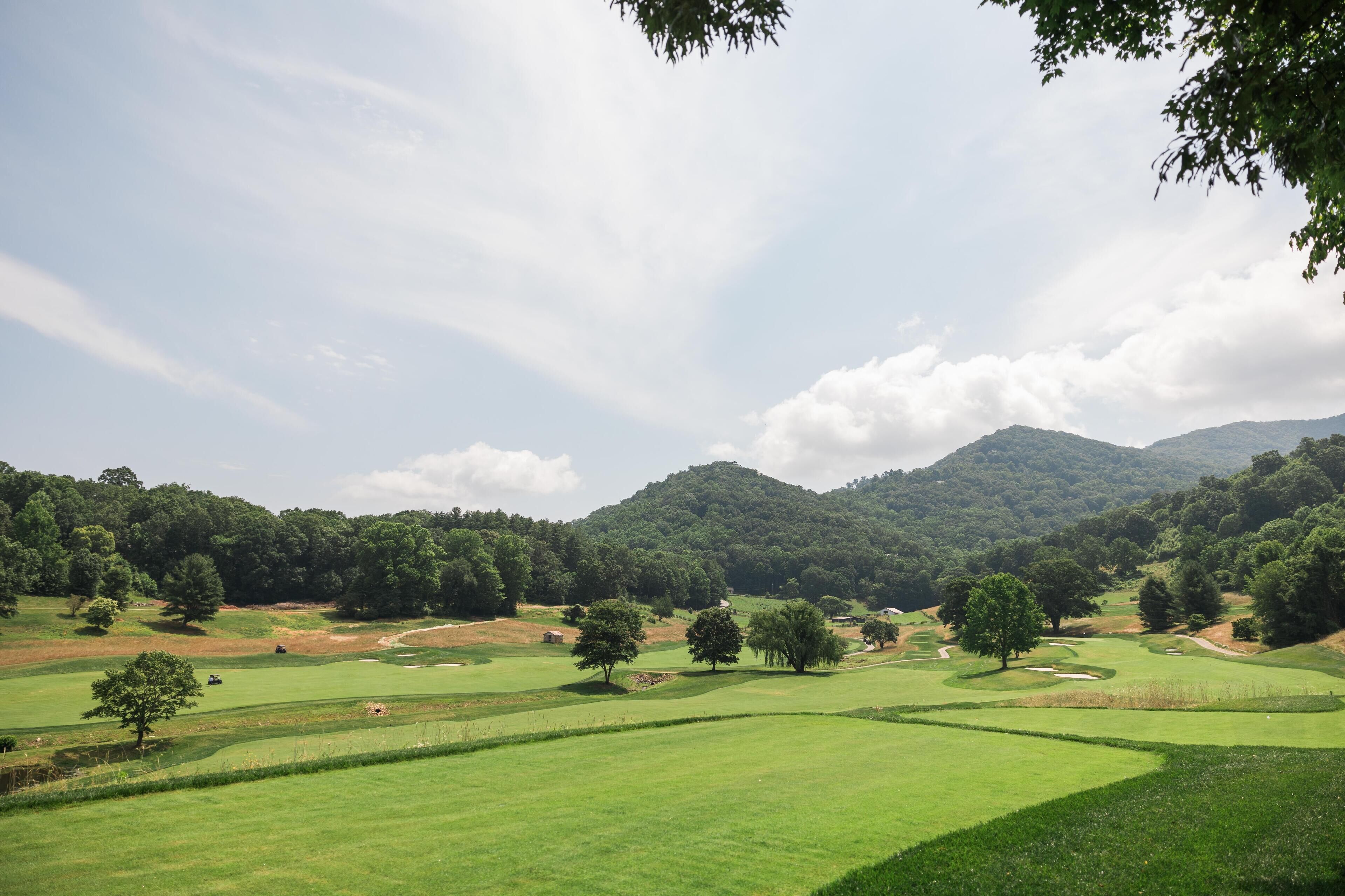 A golf course with rolling hills, trees, and a mountain in the background.