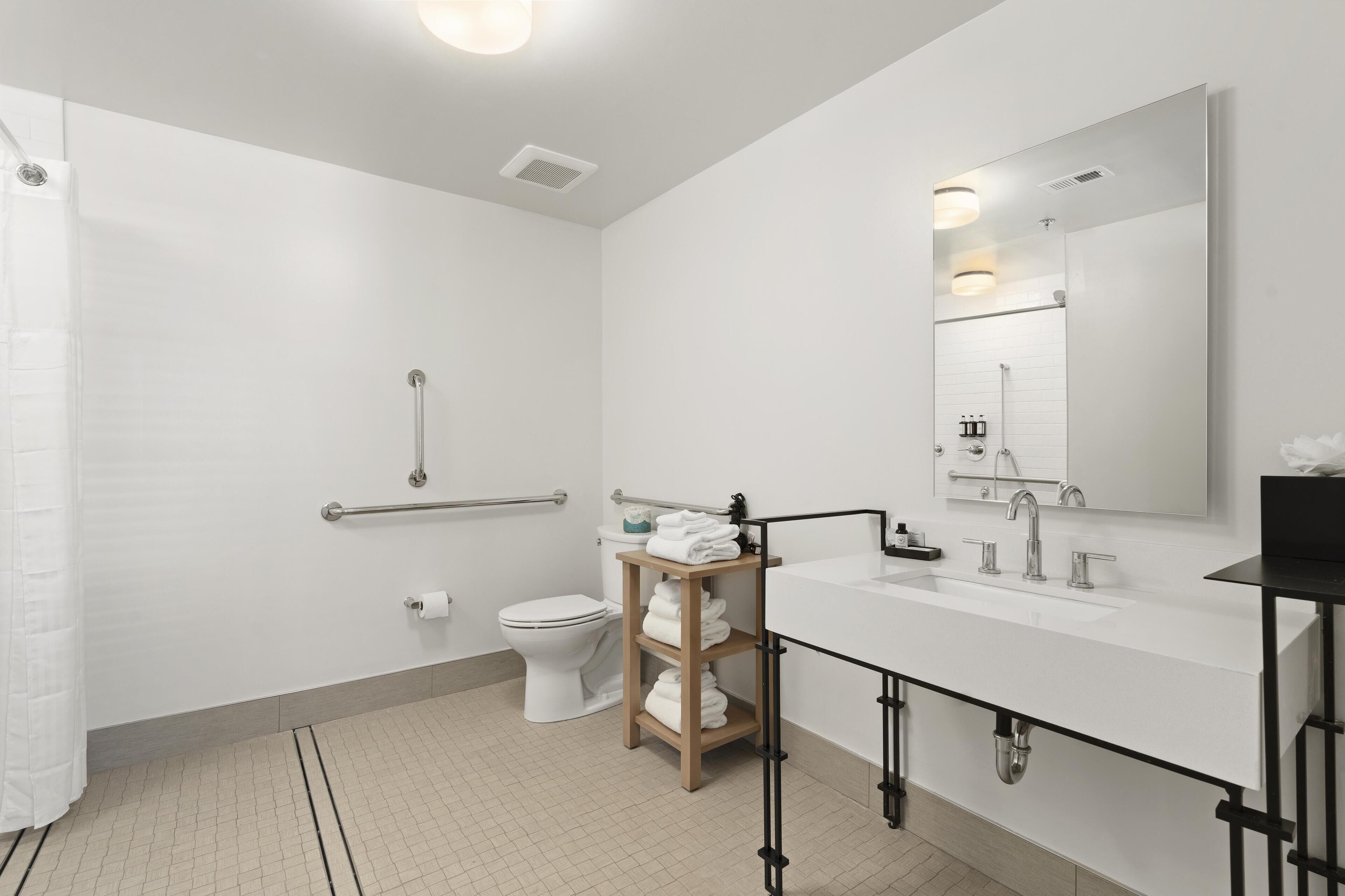 Een moderne badkamer met een wit wastafelmeubel, spiegel en toilet. Er is een douchegedeelte met een glazen deur en een handgreep.