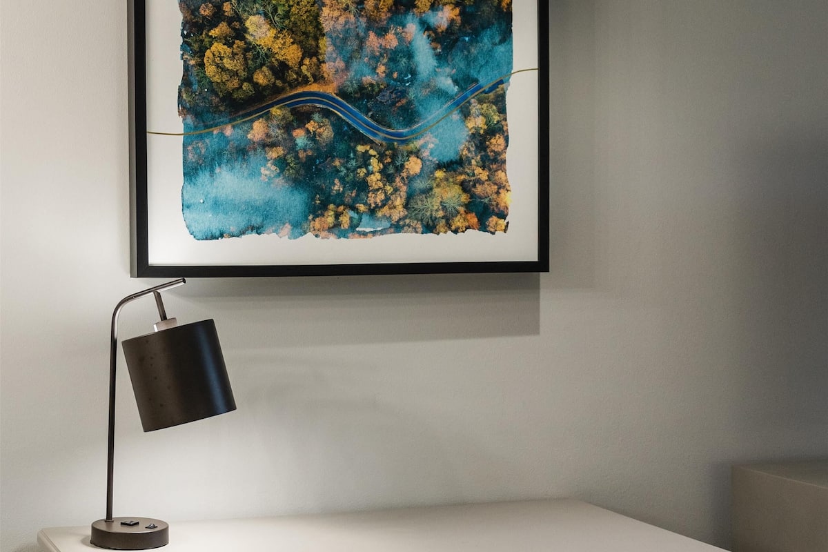 A desk with a chair, a framed abstract painting, and a desk lamp.