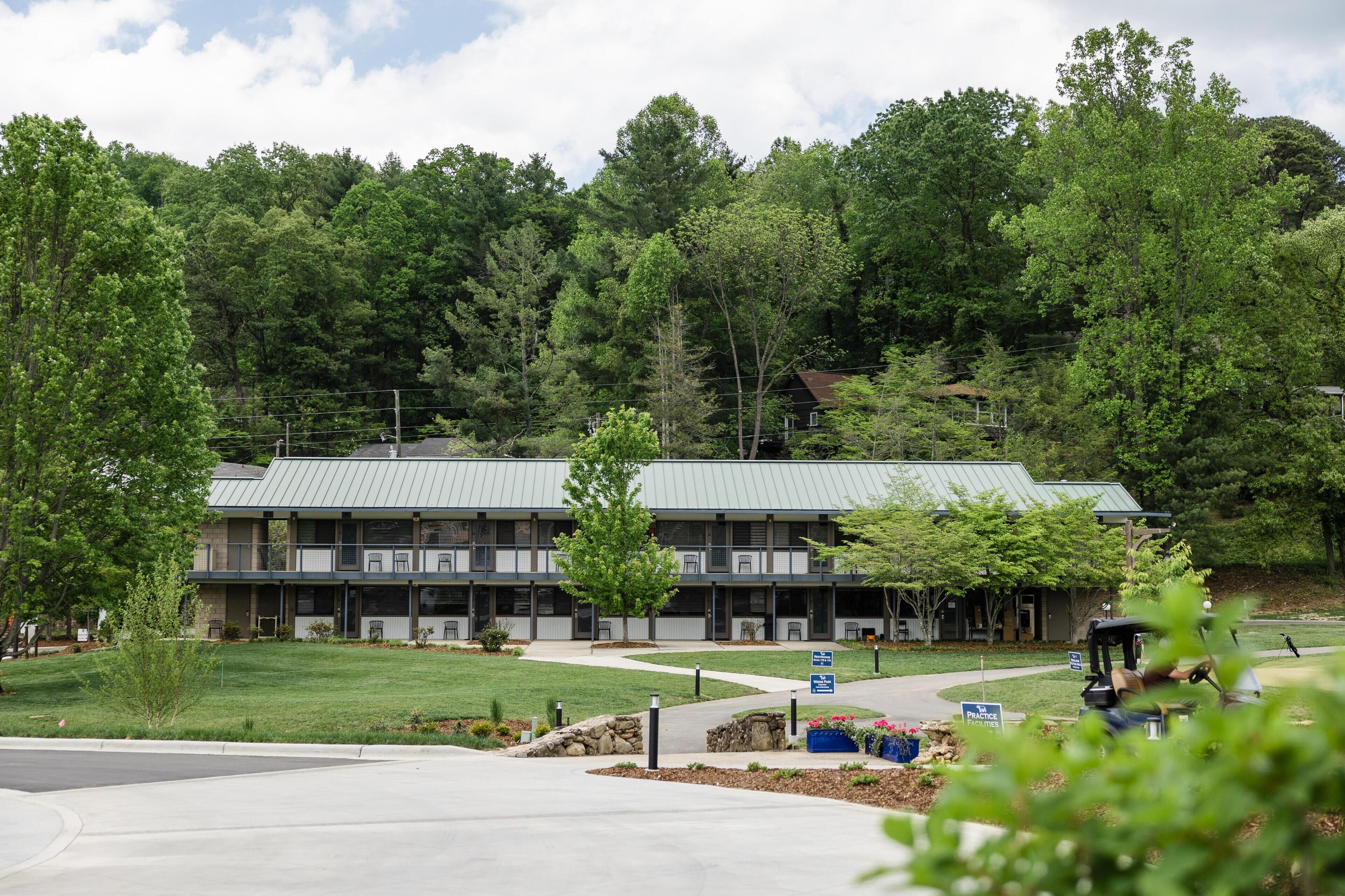 A multi-story building with a green roof, surrounded by trees and a well-maintained lawn.