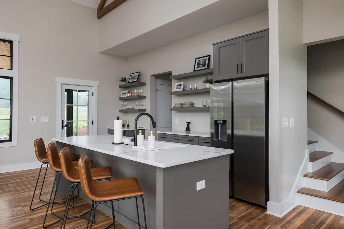 A modern kitchen with a large island, bar stools, a stainless steel refrigerator, and built-in shelves.