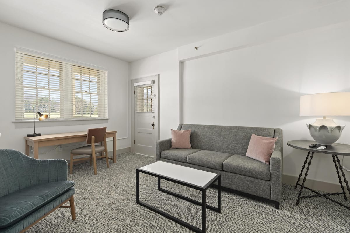 A modern living room with a grey sofa, a blue armchair, a white coffee table, and a round side table with a lamp.