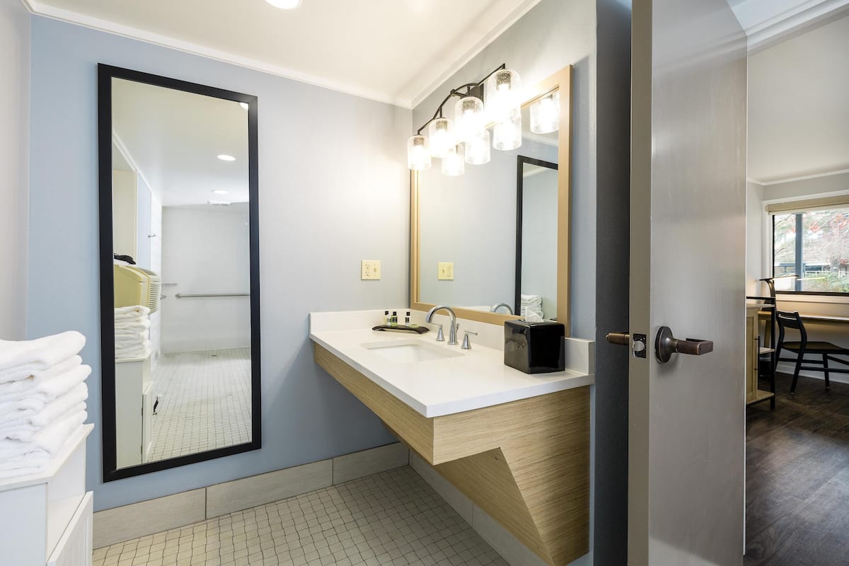 A modern bathroom with a large mirror, white sink, and wooden vanity.