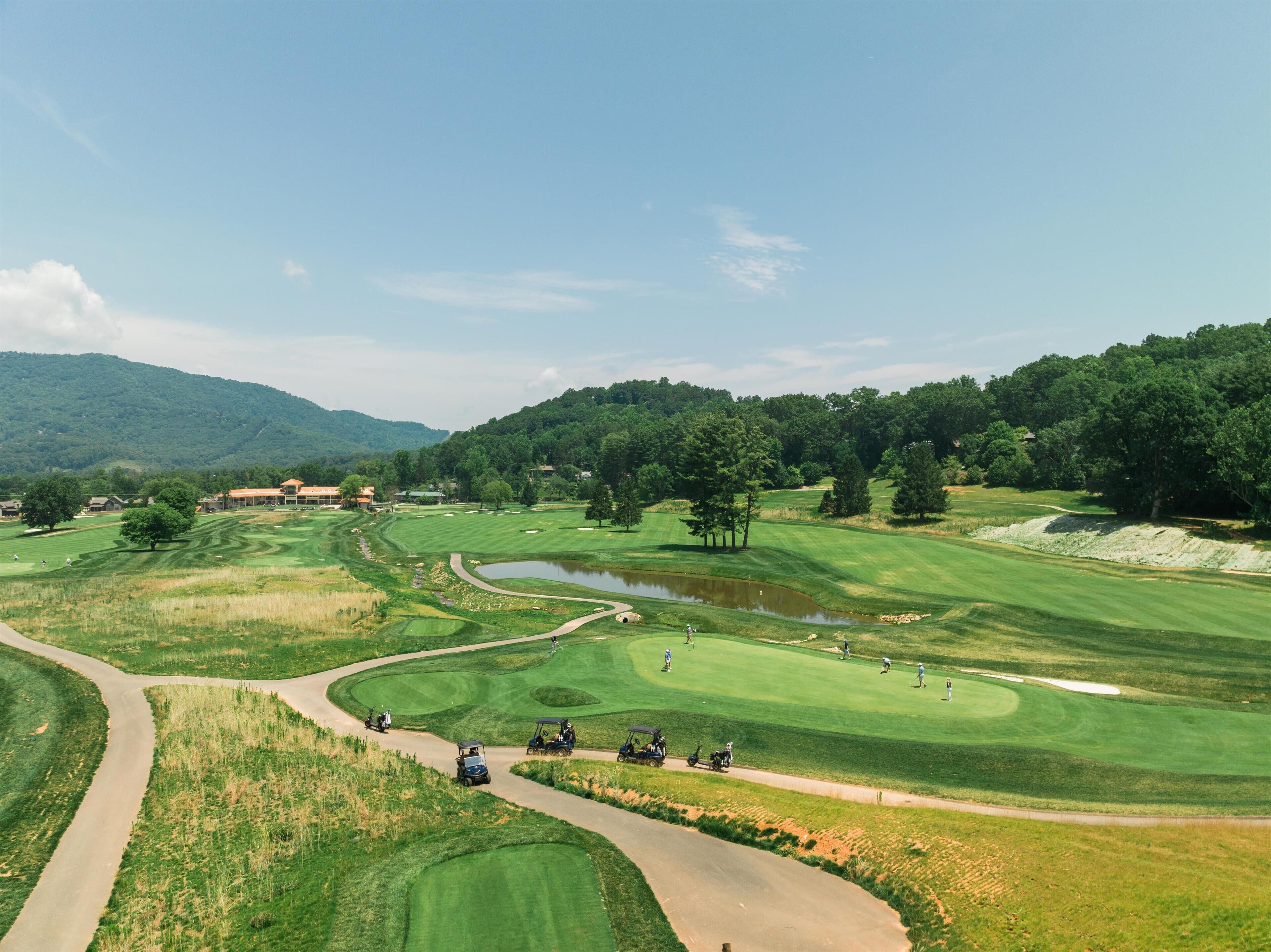 A golf course with a winding path, a pond, and a clubhouse in the background.