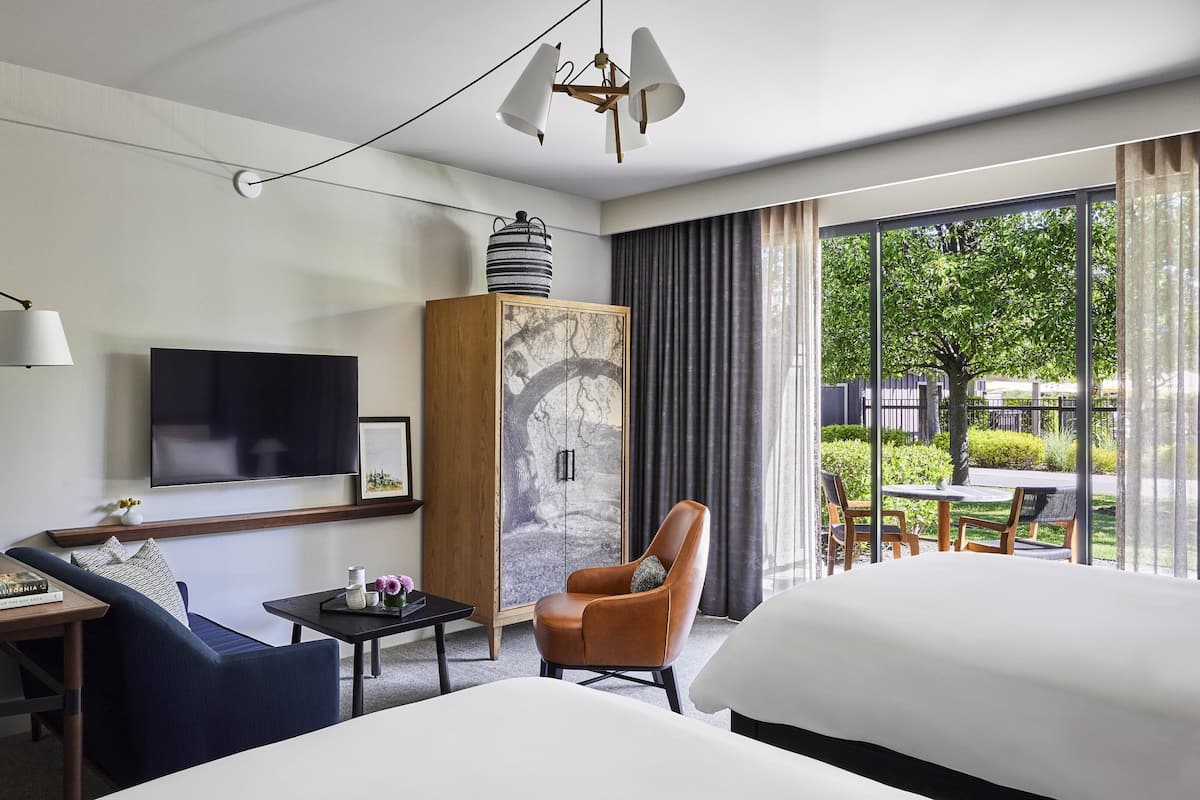 Habitación de hotel con televisor, un mueble decorado con un diseño de árbol, una silla, una cama y vistas al exterior.