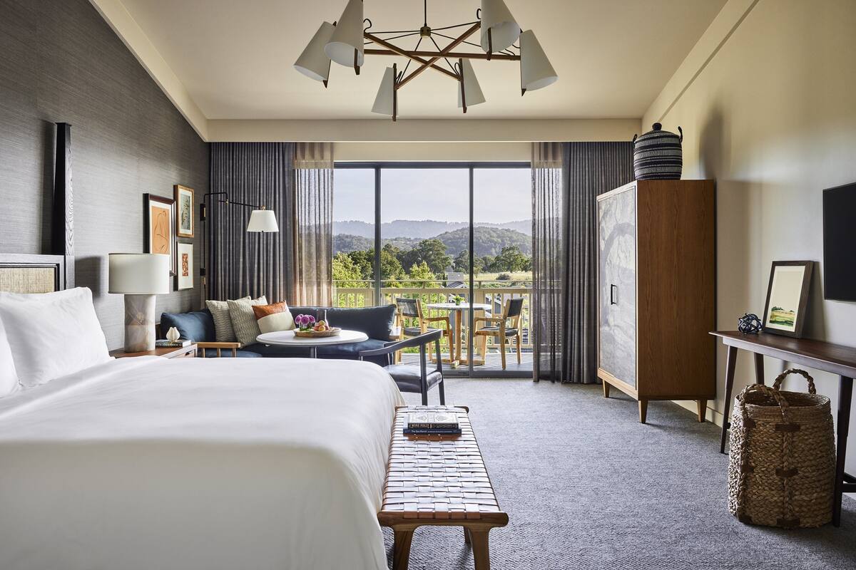 Habitación de hotel con una cama grande, un escritorio, una silla, una mesita y vistas al exterior.