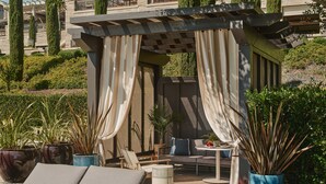 Een zonnig terras met lounge stoelen, een bijzettafeltje en potplanten.