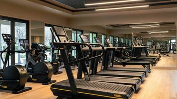 Un gimnasio con varias cintas de correr y bicicletas estáticas, ventanas amplias y piso de madera.