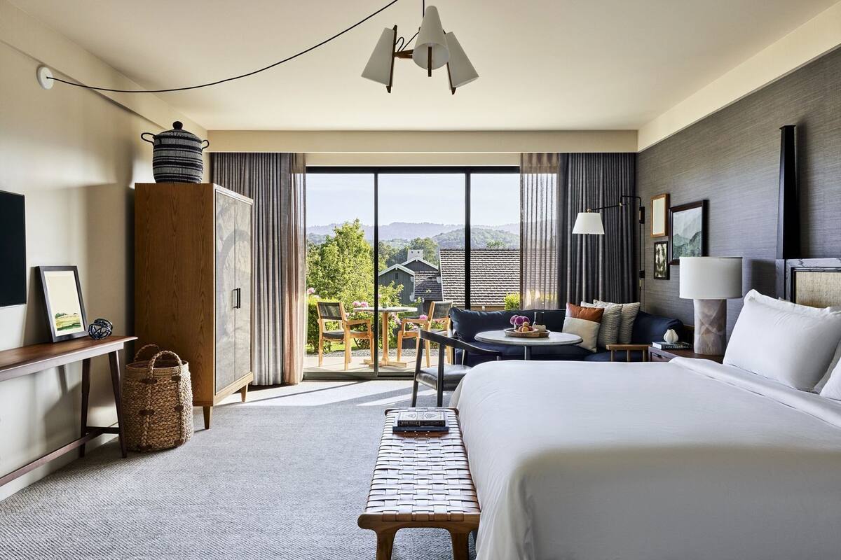 Habitación de hotel con cama, escritorio, silla, mesita, lámpara y vistas al exterior.