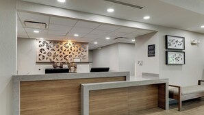 A reception desk with a modern design, featuring a wooden panel and a geometric wall decoration. There is a bench to the right and a framed picture on the wall. - Candlewood Suites Lexington by IHG (Lexington)
