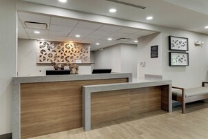 Un mostrador de recepción de diseño moderno, con un panel de madera y un adorno mural geométrico. A la derecha hay un banco y un cuadro enmarcado en la pared.