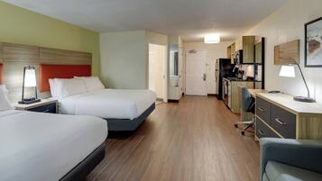Een hotelkamer met twee bedden, een bureau, een stoel, een kitchenette en een badkamer.
