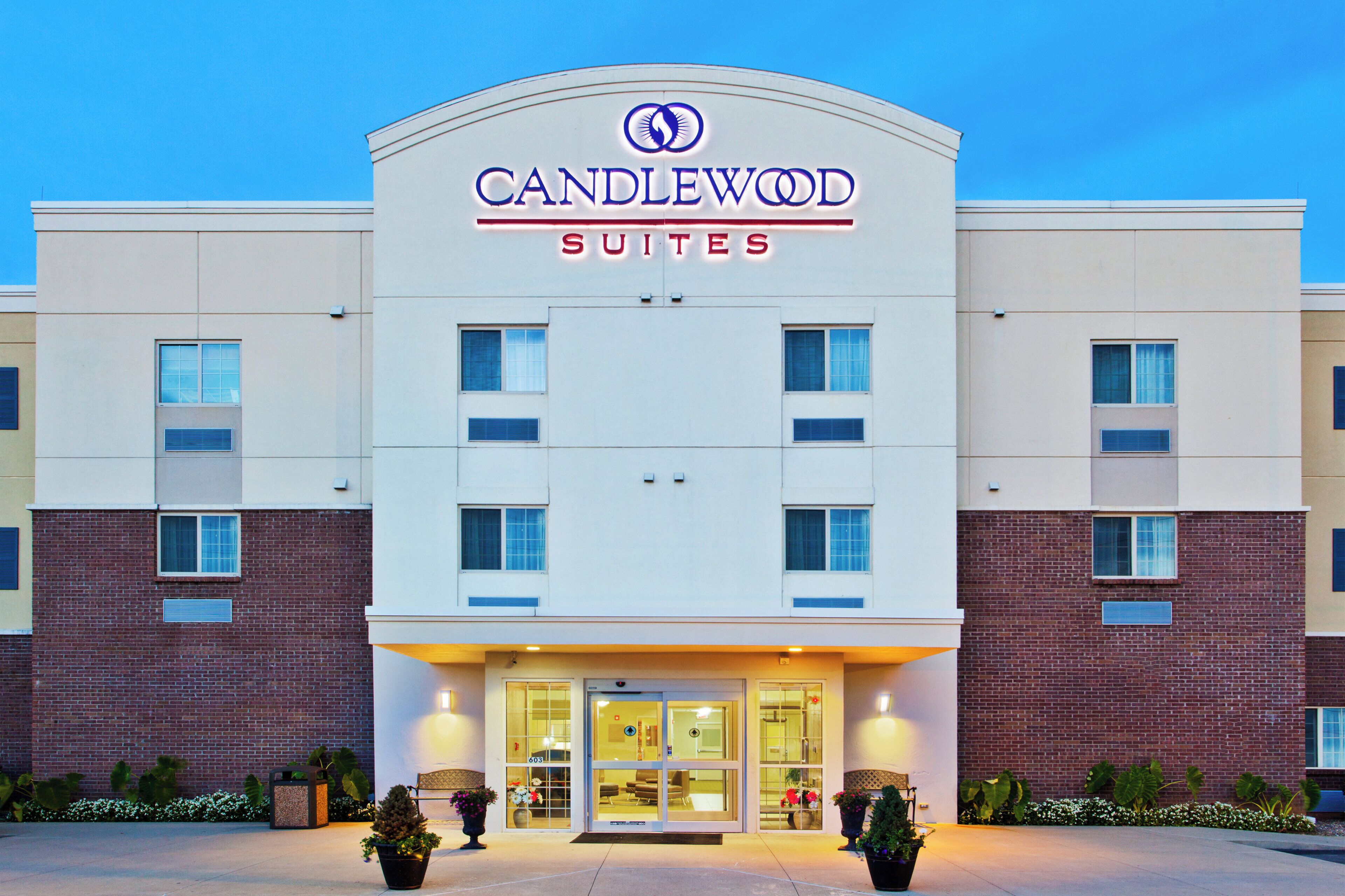 A hotel with a modern facade, a prominent sign reading 'CANDLEWOOD SUITES,' and a well-lit entrance with a glass door.