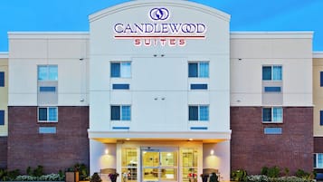 A hotel with a modern facade, a prominent sign reading 'CANDLEWOOD SUITES,' and a well-lit entrance with a glass door.