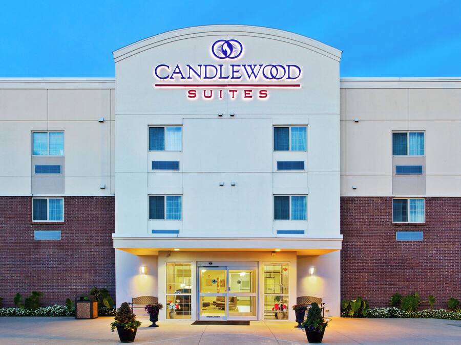 Um hotel com fachada moderna, um letreiro grande com a inscrição 'CANDLEWOOD SUITES' e uma entrada bem iluminada com porta de vidro.