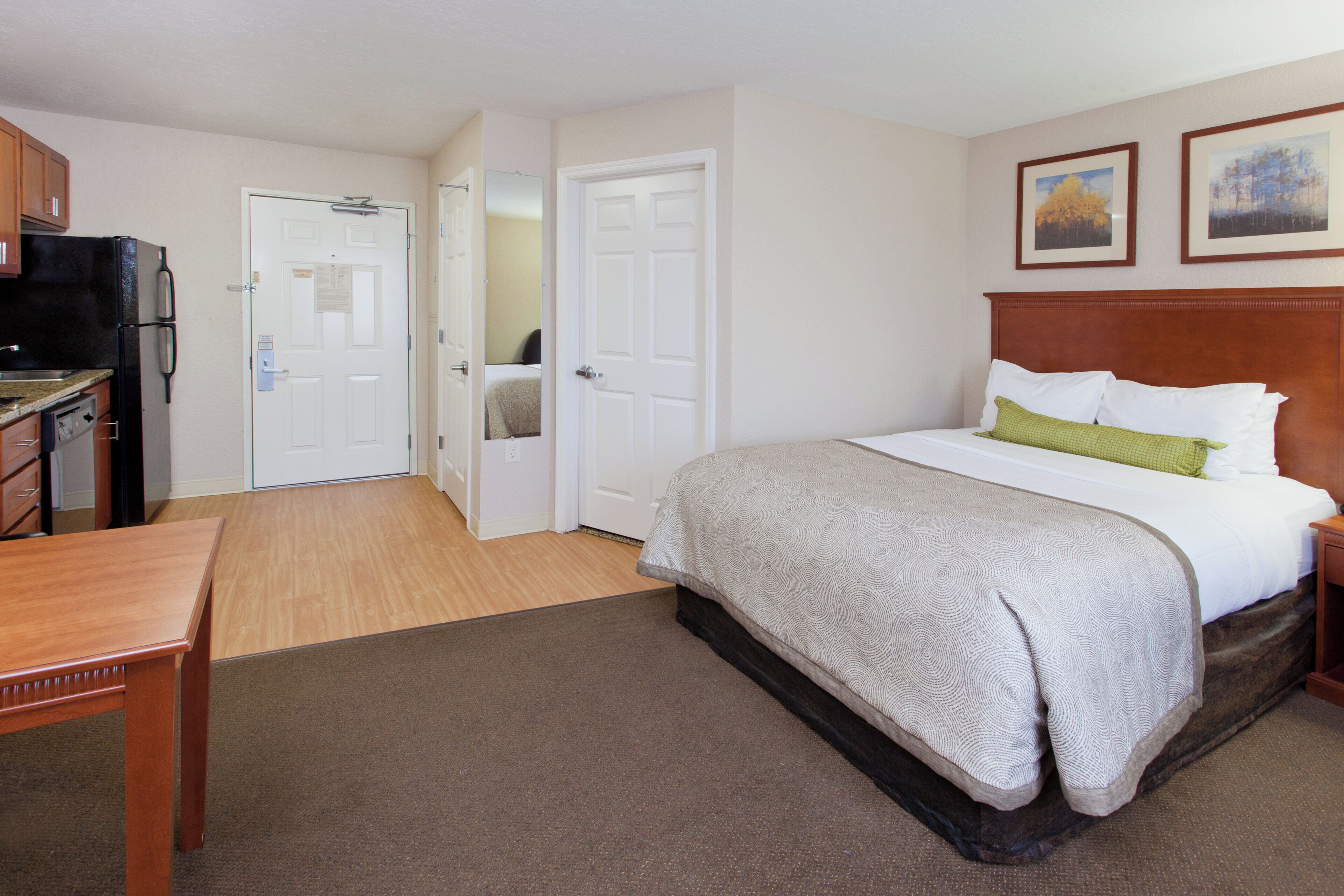A hotel room with a bed, a desk, a refrigerator, and two doors.