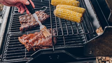 Uma churrasqueira com carne e milho assando.