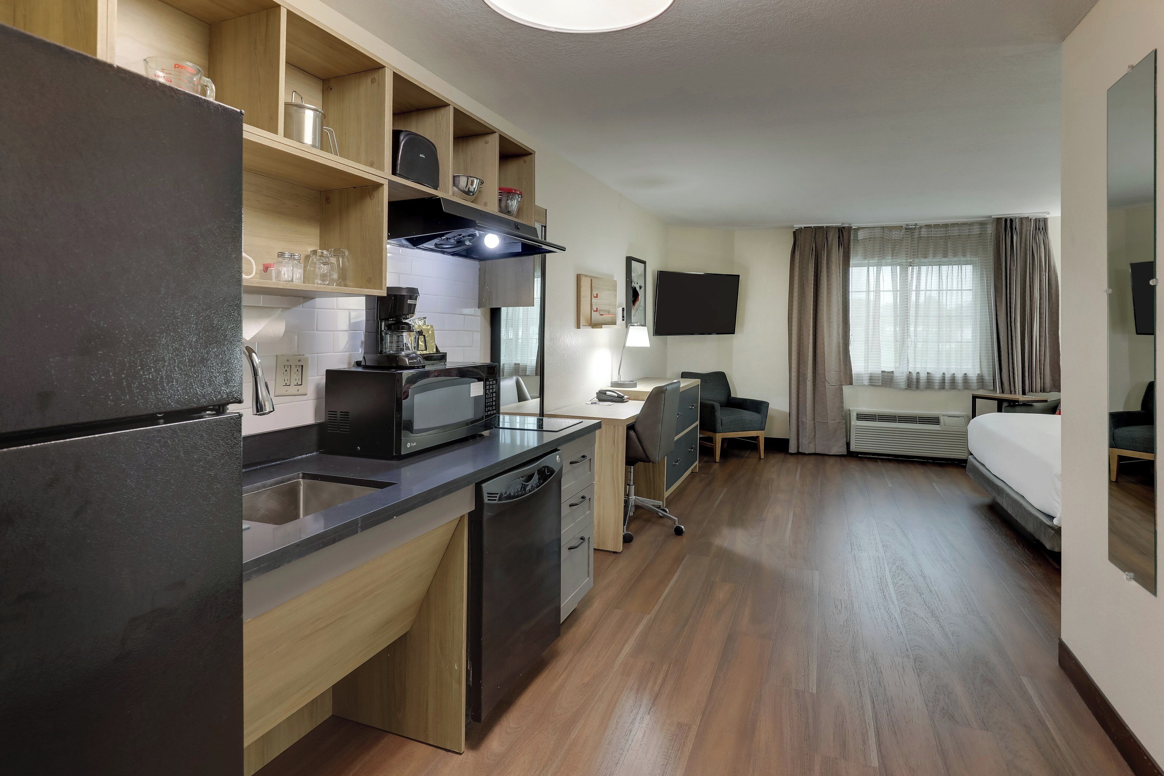A compact hotel room with a kitchenette, a bed, a desk, and a television.