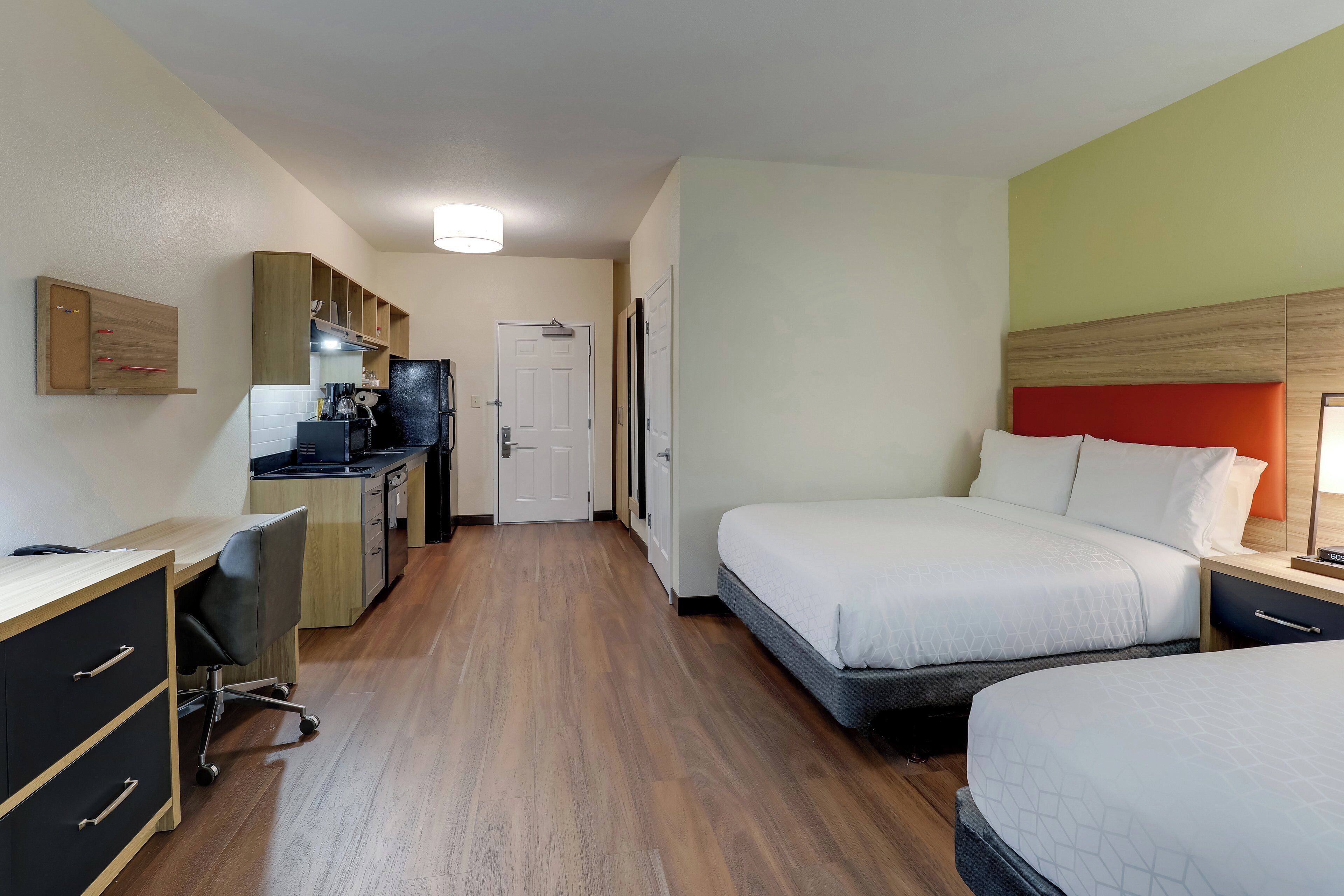 Una habitación de hotel con escritorio, kitchenette y dos camas.
