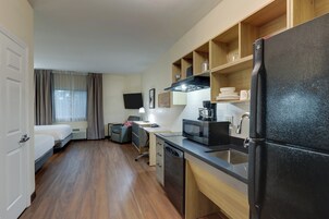 Una habitación de hotel compacta con kitchenette, una cama, un escritorio y un televisor.