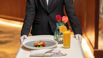Un serveur en costume noir apporte une assiette de nourriture et un verre de jus d’orange à une table.