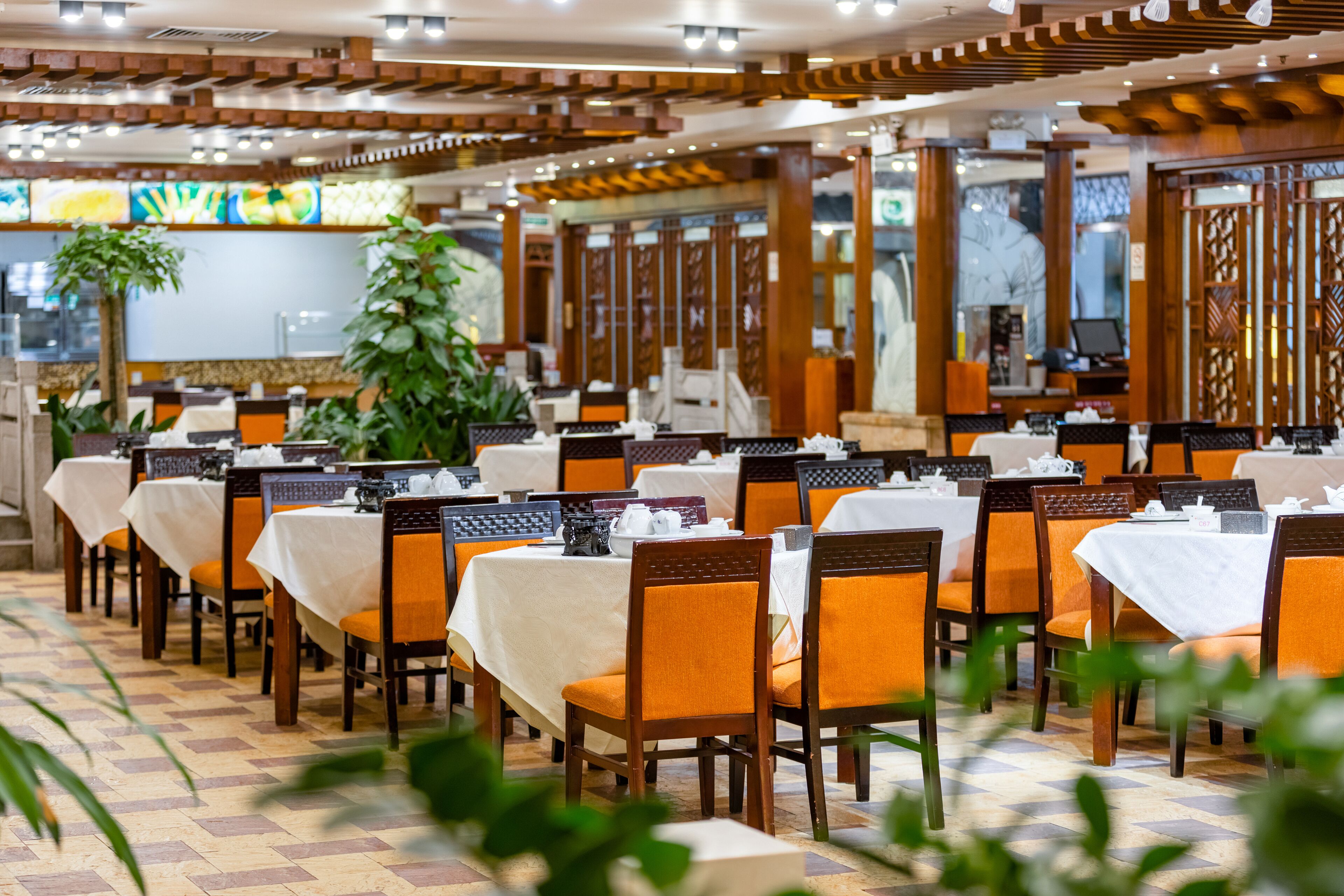 Un restaurant doté de nombreuses tables et chaises, de plantes d’intérieur et d’un sol carrelé.