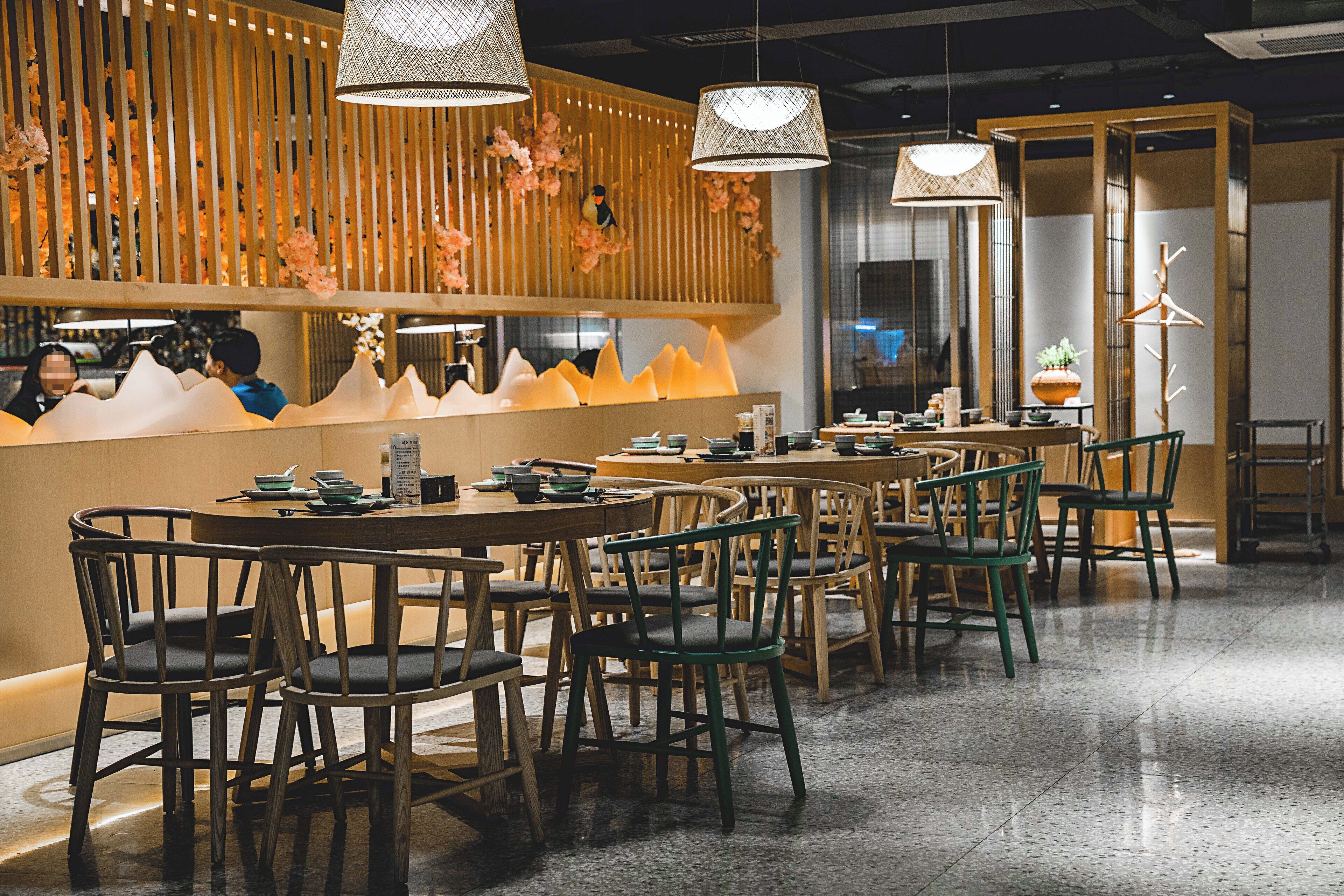 A restaurant interior with wooden furniture, pendant lighting, and a decorative wall.