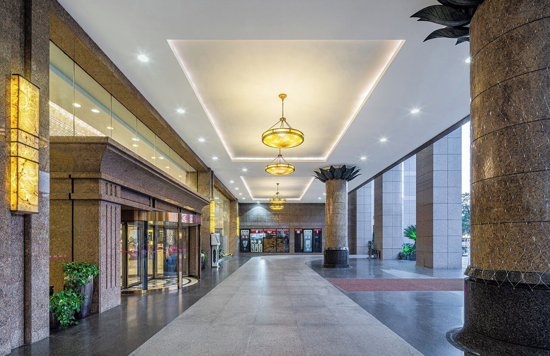 A spacious corridor with a modern ceiling design, large pillars, and a glass storefront on the left.