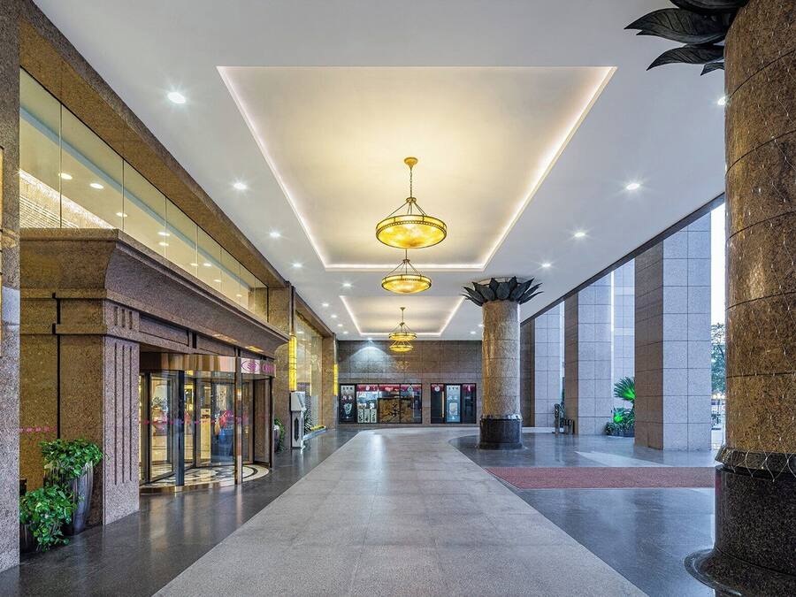 A spacious corridor with a modern ceiling design, large pillars, and a glass storefront on the left.