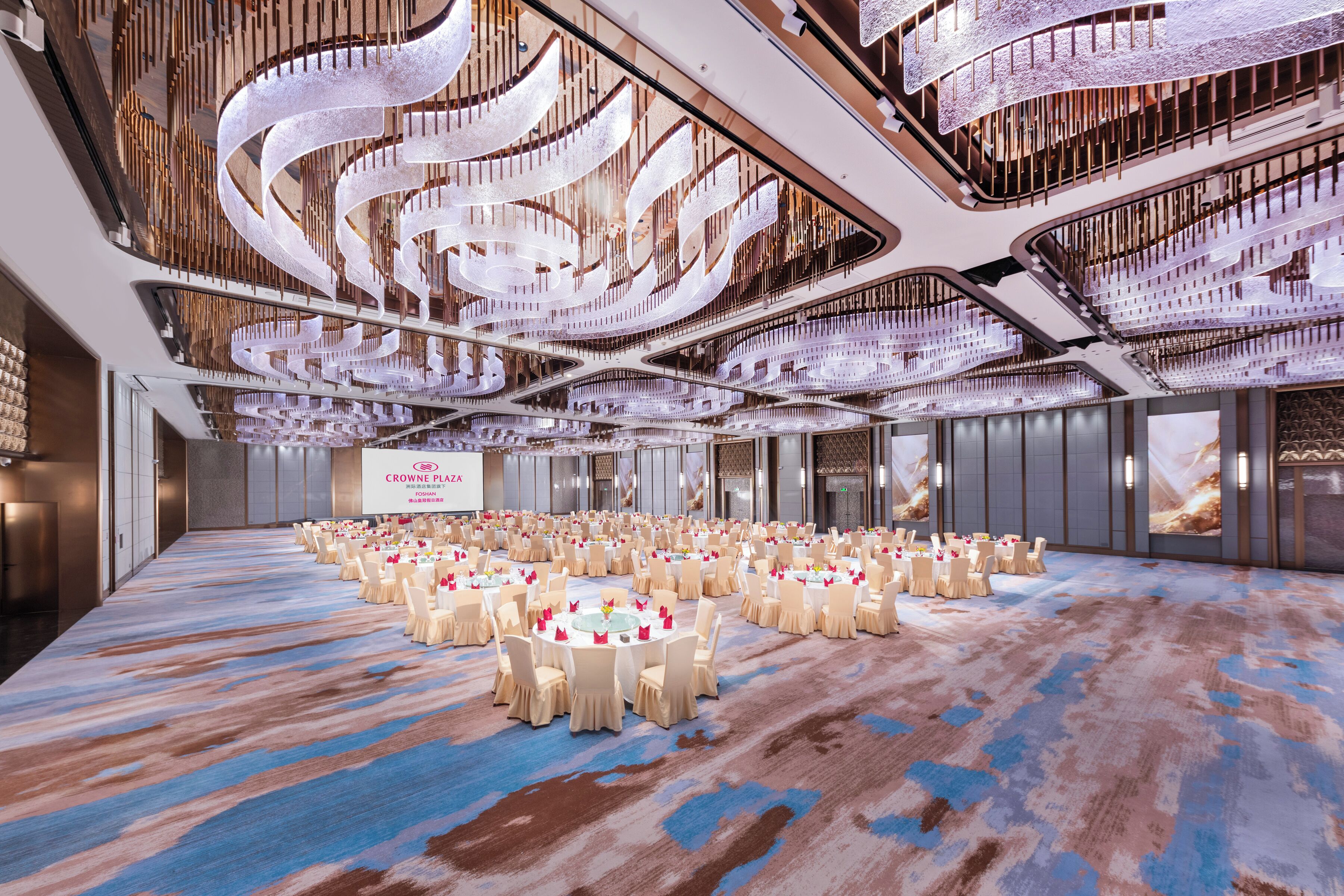 A large conference room with multiple round tables, each set with white chairs and small centerpieces.