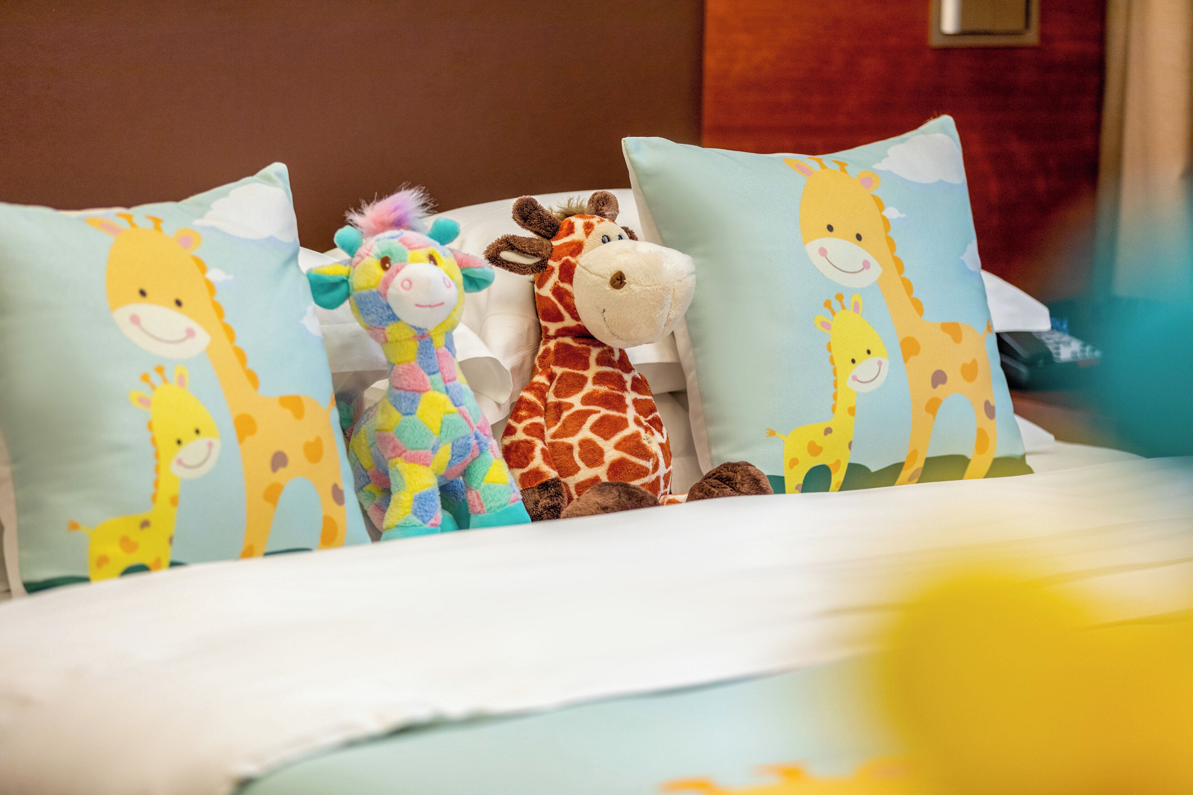A bed with three giraffe-themed pillows and a stuffed giraffe toy.